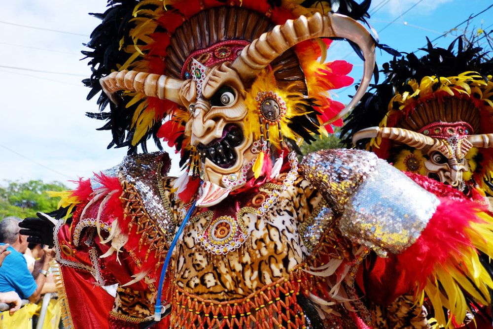 Diablo Cojuelo con máscara artesanal y traje colorido durante una celebración del carnaval dominicano.